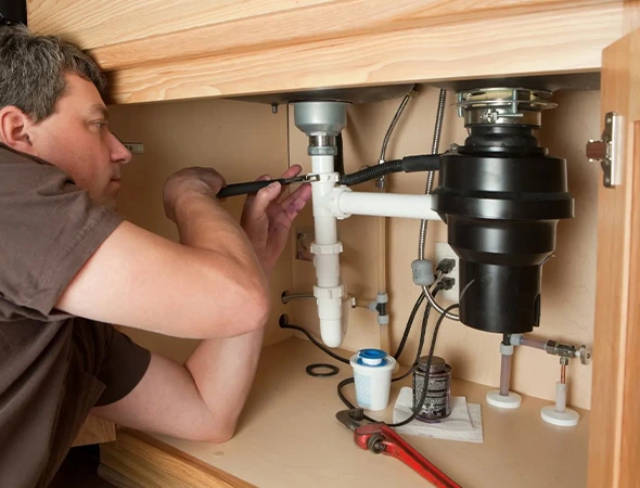 Plumber installing a new garbage disposal unit under a kitchen sink in Coconut Creek, FL